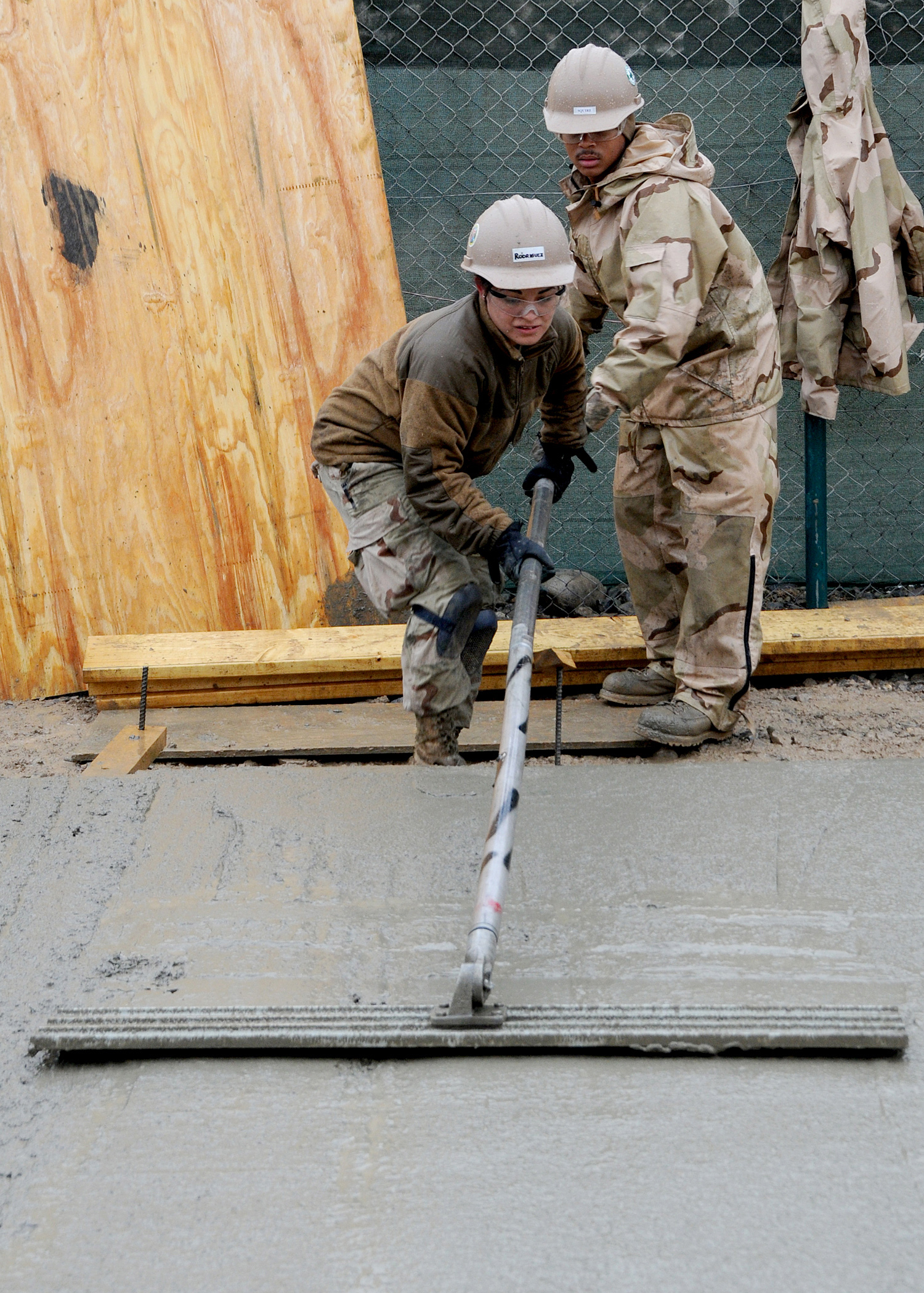 Two workers using a long-handled bull float to level a freshly poured concrete slab.