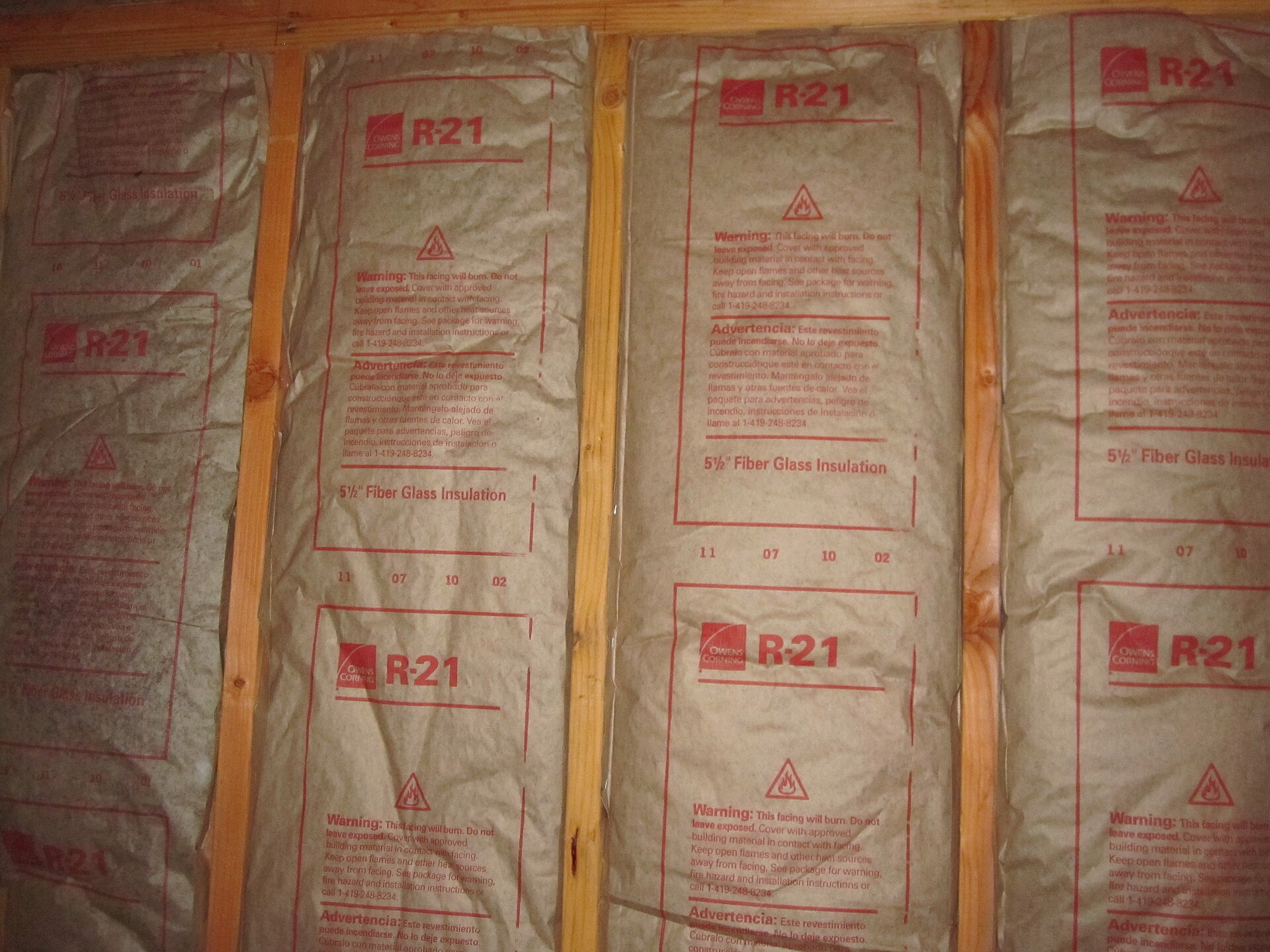 Kraft-faced Owens Corning fiberglass batt insulation fitted between wooden wall studs.